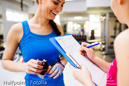 Woman in gym, personal trainer, consultiing plan on clipboard