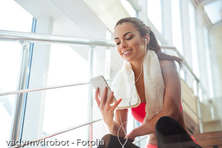 Cheerful woman sitting in gym and listening to music