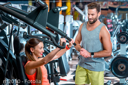 Young woman with personal trainer exercising on the simulator in the gym. Sport couple training together