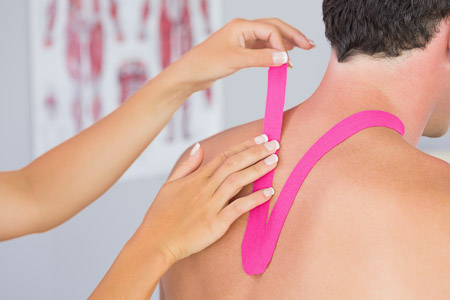 Physiotherapist putting on pink kinesio tape on male patients neck