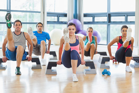 Instructor with fitness class performing step aerobics exercise