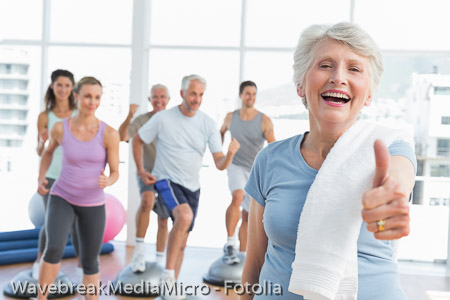 Senior woman gesturing thumbs up with people exercising