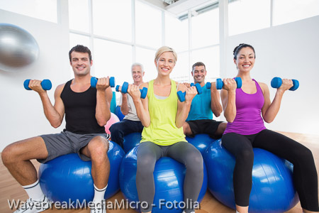 People sitting on balls and lifting weights in fitness club