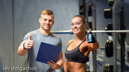 smiling young woman with personal trainer in gym