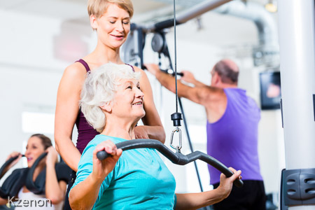 Senior woman doing back training with trainer in gym