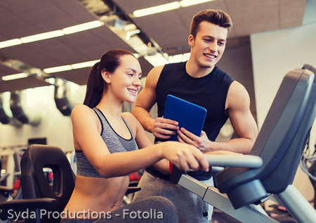 happy woman with trainer on exercise bike in gym